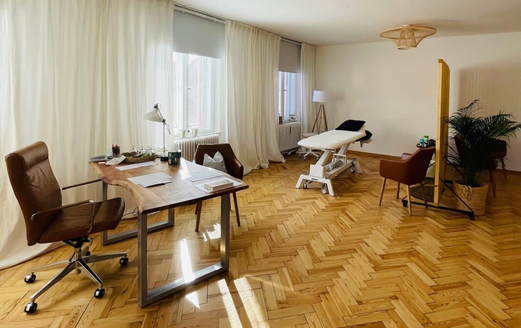 Behandlungsraum der Praxis Sandra Liebold mit Schreibtisch, Therapieliege und Fischgrätparkett