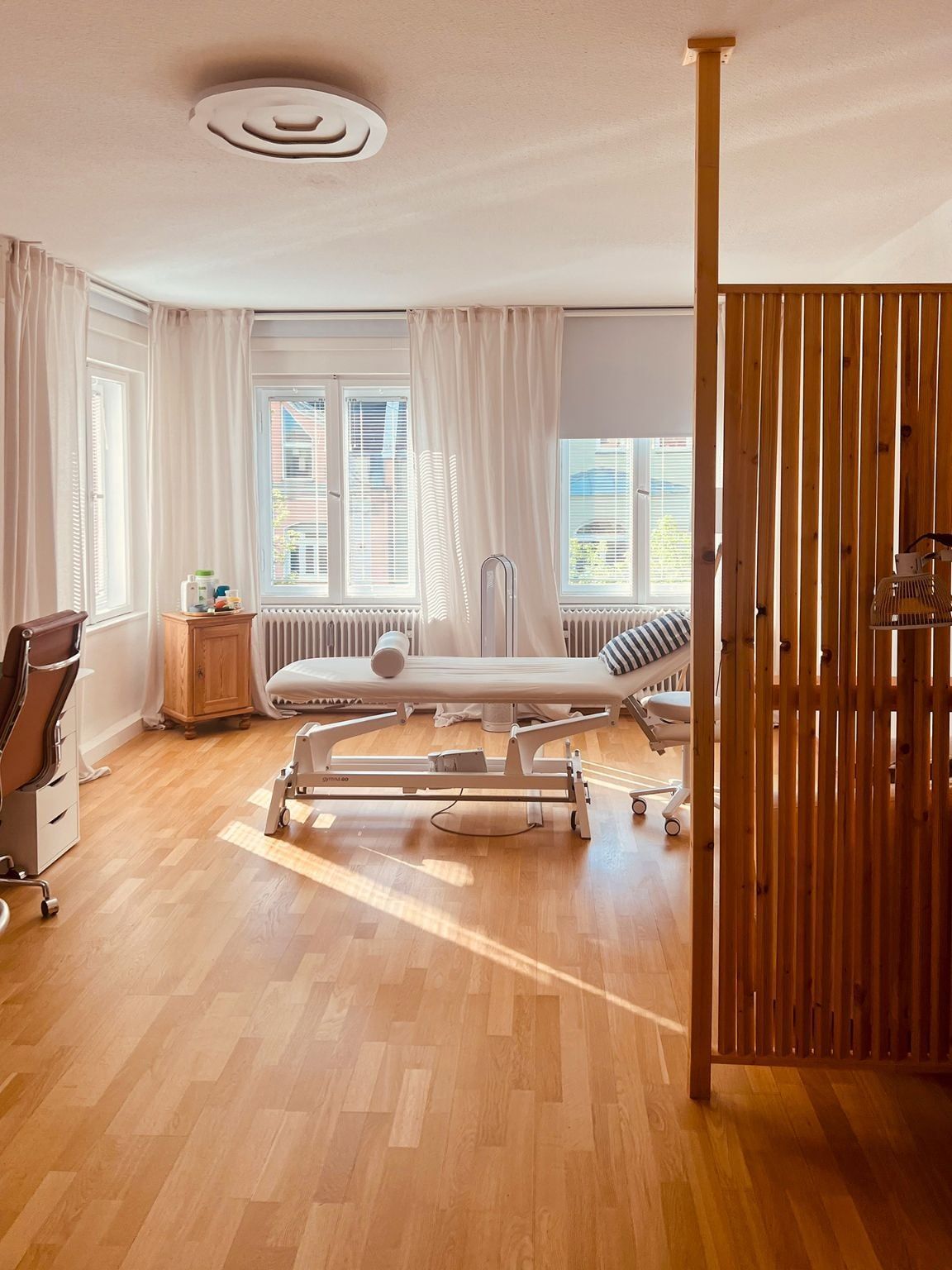 Heller Behandlungsraum mit Therapieliege und Raumteiler aus Holz