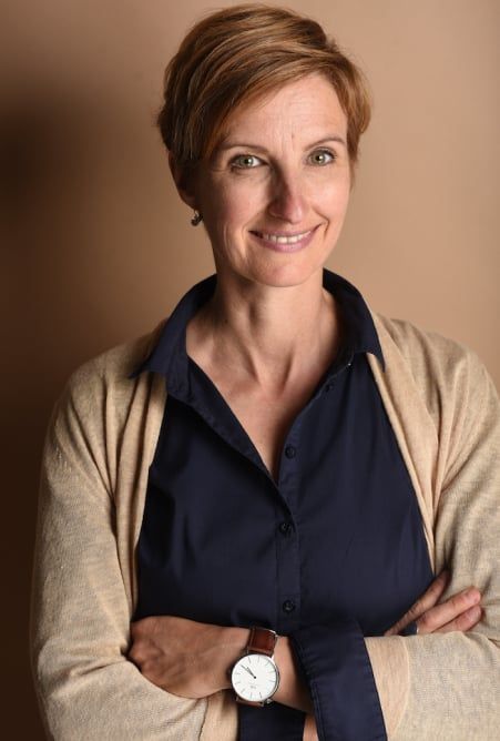 Sandra Liebold mit verschränkten Armen vor beigem Hintergrund, sie lächelt in die Kamera